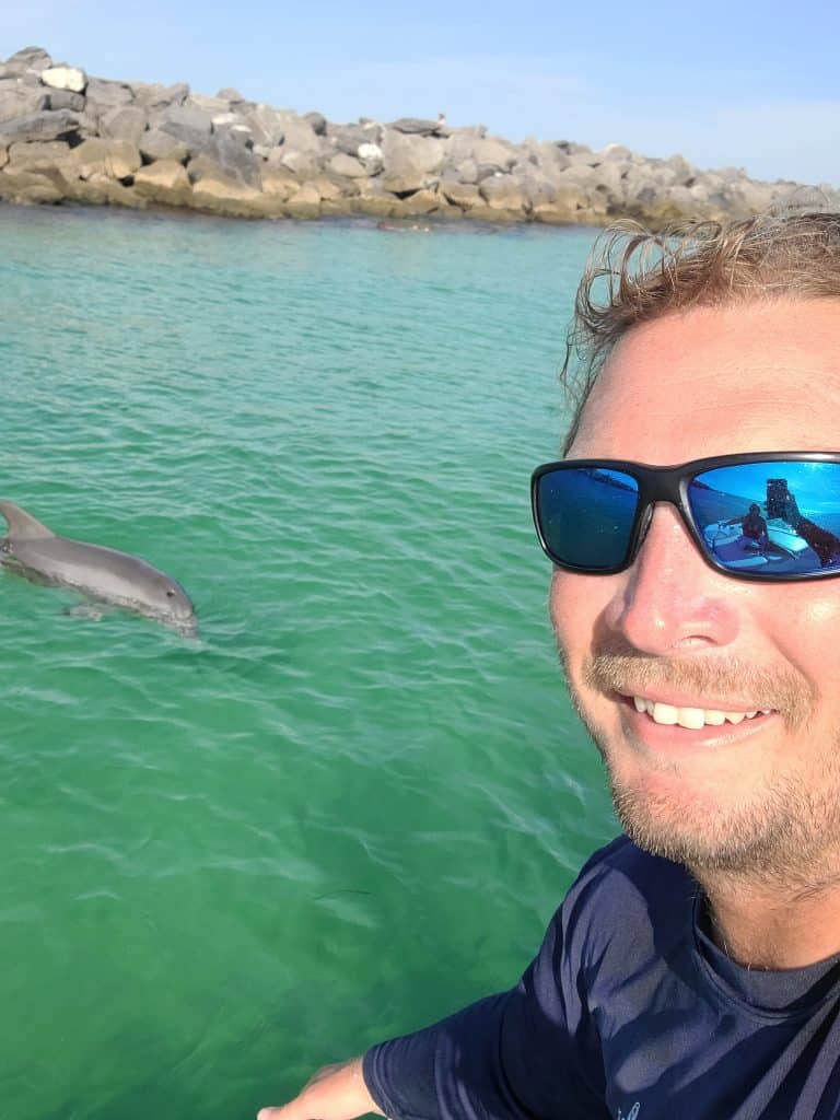 Crew member from Anchor Charters taking a selfie with a dolphin while captaining a private boat tour in Panama City Beach Florida