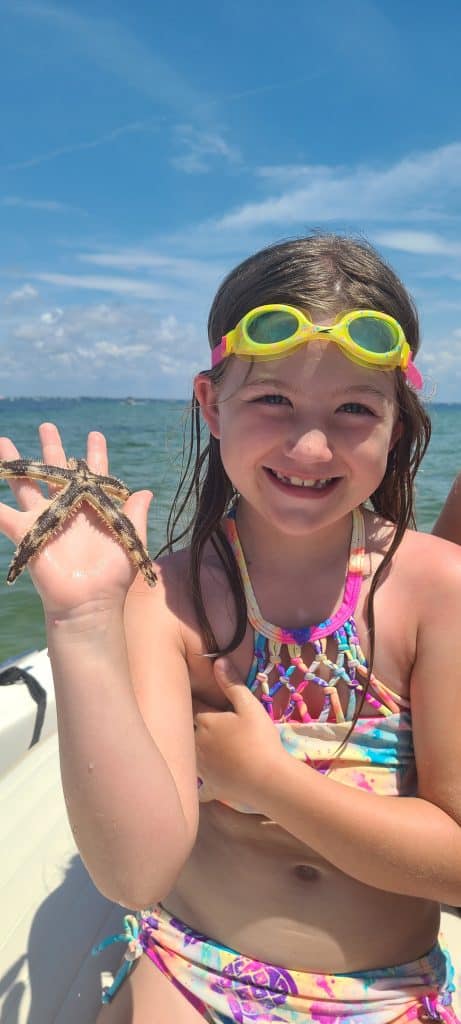 Little girl holding a star fish she found while on a private boat tour with Anchor Charters in Panama City Florida