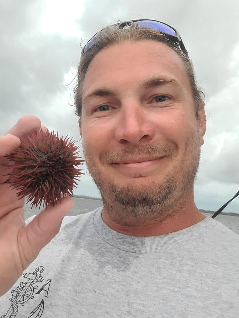 Crew member from Anchor Charters holding up a sea urchin while captaining a private boat tour in Panama City Beach Florida