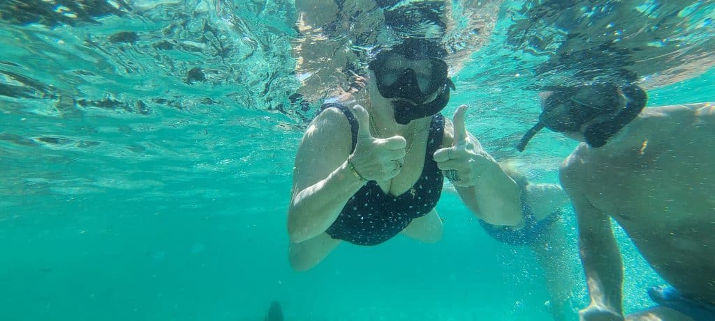 Woman and a man in a snorkel giving a thumbs up to the camera under water